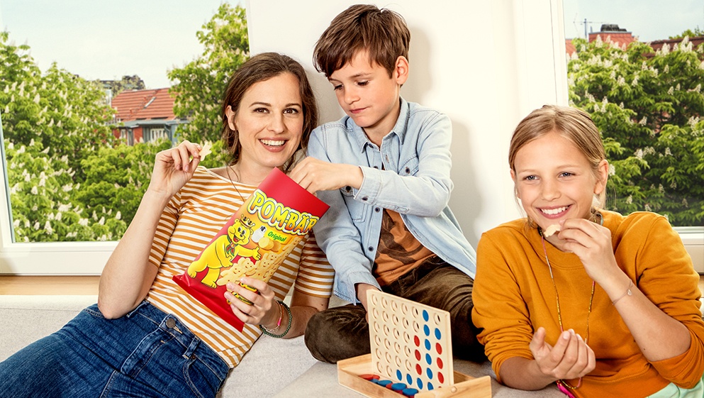 A mother plays with her son and daughter, snacking POM-BEARS